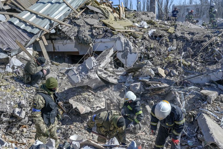 Tentara Ukraina dan petugas penyelamat mencari jenazah yang tertimbun reruntuhan barak militer setelah dihantam roket Rusia di Mykolaiv, Ukraina selatan, Jumat (19/3/2022) pagi. Media Ukraina melaporkan bahwa pasukan Rusia mengerahkan serangan udara skala besar di Mykolaiv, sedikitnya menewaskan 50 orang.