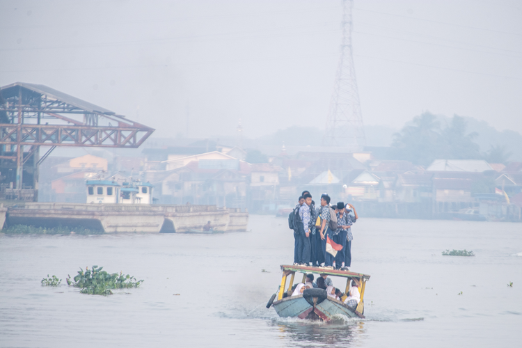 Sejumlah pelajar berangkat sekolah menggunakan perahu tradisional melewati kawasan yang diselimuti kabut asap di Sungai Ogan, Palembang, Sumatera Selatan, Rabu (6/9/2023). Kabut asap tersebut merupakan dampak dari kebakaran hutan dan lahan yang terjadi di berbagai kabupaten di Sumatera Selatan. 