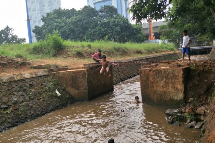 Anak-anak bermain air di Kali Baru Barat di Jalan Raya Pasar Minggu, Mbau, Pancoran, Jakarta Selatan, Kamis (26/7/2018) siang. Seorang anak tampak lompat dari besi penghubung dua sisi kali ke dalam air.