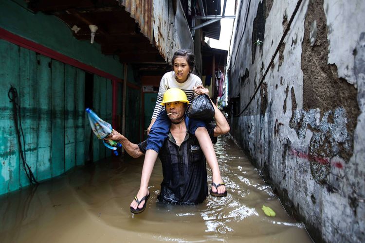 Seorang bapak dengan anaknya melintasi lorong kecil saat banjir di Jalan Karet Pasar Baru, Karet Tengsin, Jakarta Pusat, Selasa (25/2/2020). Hujan deras sejak Senin dini hari membuat sejumlah daerah di Ibu Kota tergenang banjir.
