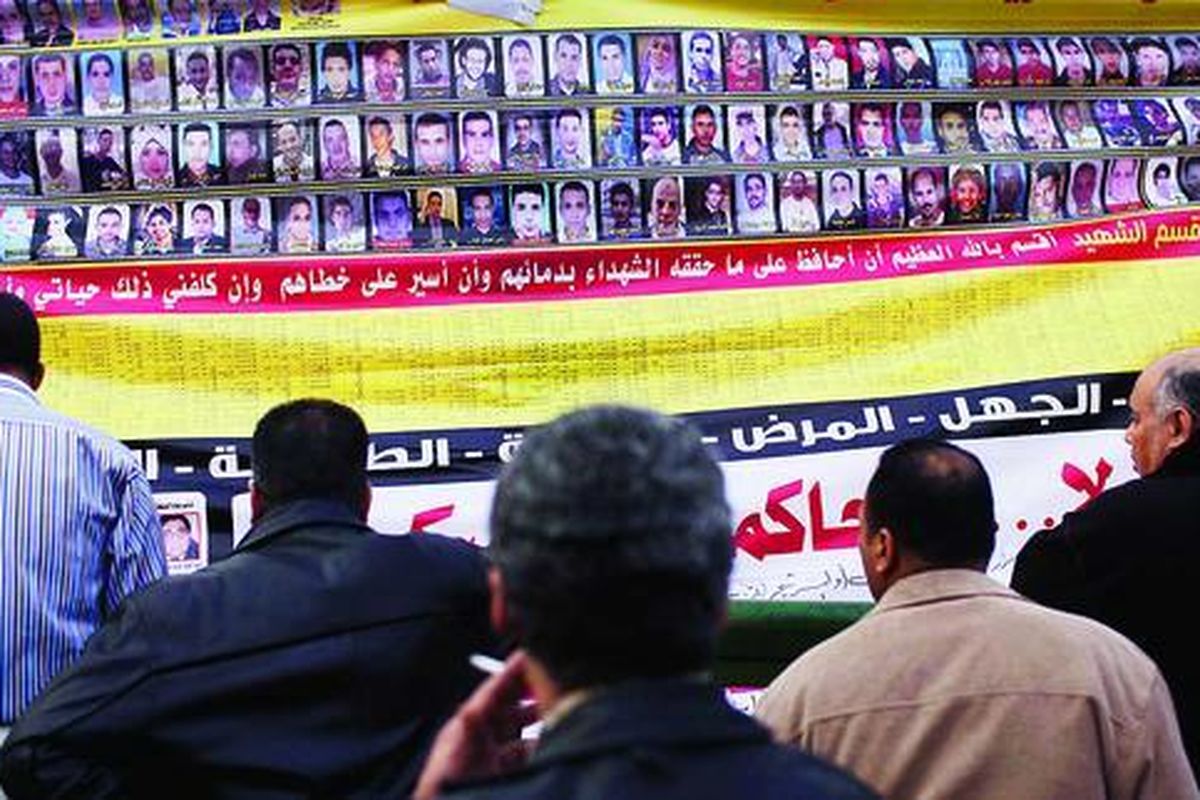 Sejumlah pria  melihat spanduk yang memajang foto orang-orang yang tewas dalam kerusuhan terakhir di Alun-alun Tahrir, Kairo, Mesir, Minggu (27/11). Di bawah spanduk itu tertulis kalimat berbahasa Arab 