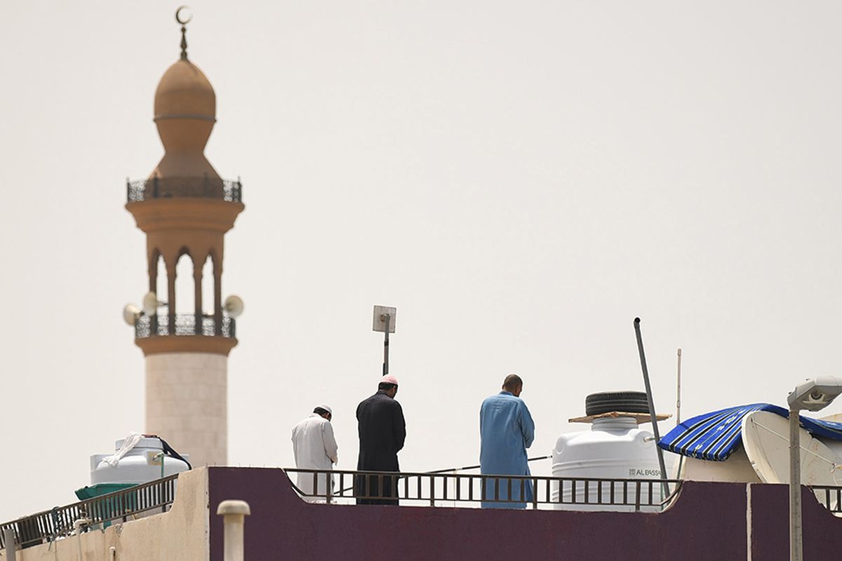 Sejumlah pekerja melakukan shalat di atap sebuah bangunan tempat tinggal di dekat sebuah masjid, selama pembatasan kegiatan yang diberlakukan untuk mencegah penyebaran virus corona, di Teluk Emirat, Dubai, Selasa (21/4/2020). Rasa jenuh selama masa karantina pencegahan virus corona, menjadikan area atap rumah atau apartemen banyak difungsikan warga sebagai alternatif lokasi berkegiatan.