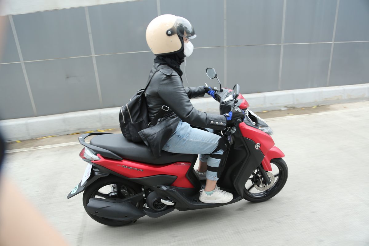 Ilustrasi perempuan naik sepeda motor.