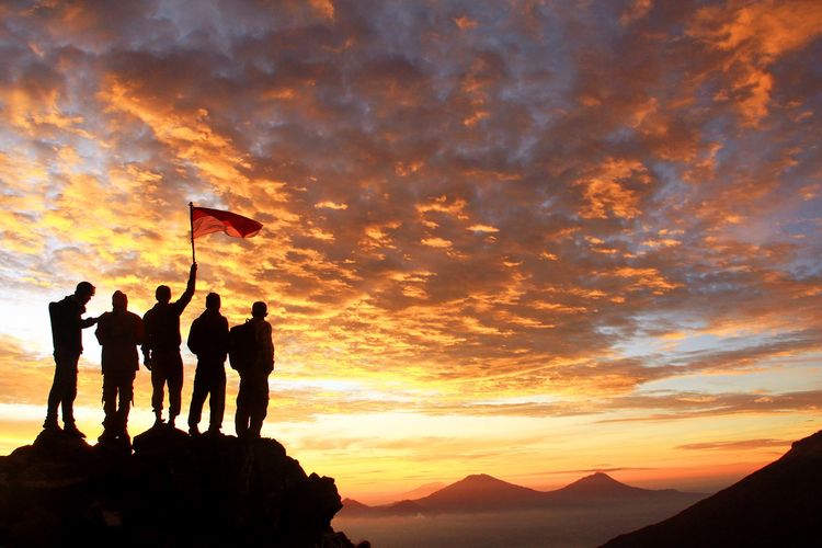 Ilustrasi pemuda. Sekelompok anak muda memegang bendera merah putih di puncak gunung, menatap matahari terbit. 