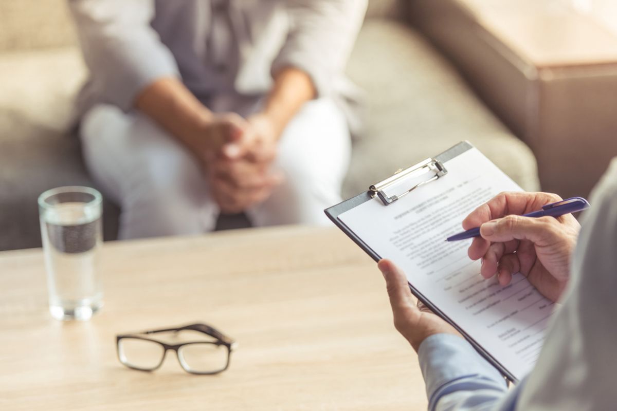 Cropped image of depressed man at the psychotherapist. Doctor is making notes while listening to his patient