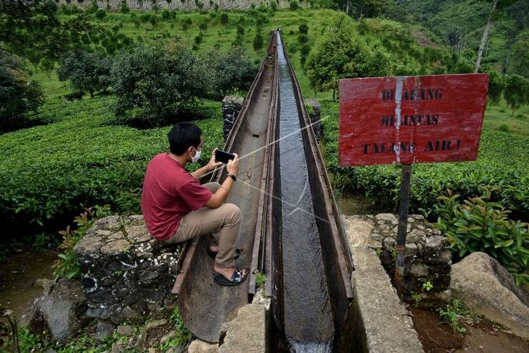 Pengunjung berswafoto di jembatan irigasi air peninggalan zaman kolonial Belanda, kawasan Perkebunan PTPN VIII Dayeuhmanggung, Cilawu, Kabupaten Garut, Jawa Barat, Jumat (22/01/2021). Jembatan irigasi air sepanjang 200 meter yang dibangun pada tahun 1913 oleh kolonial Belanda tersebut menjadi daya tarik wisatawan dengan suasana perkebunan teh dan pemandangan gunung Cikuray (ANTARA FOTO/Candra Yanuarsyah/agr/rwa).