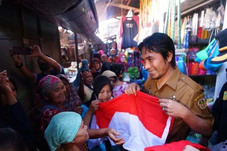 BAGI BENDERA—Bupati Madiun, Ahmad Dawami membagikan ribuan bendera merah putih gratis bagi pedagang dan pengunjung pasar Dolopo, Kecamatan Dolopo, Kabupaten Madiun, Jawa Timur, Senin (15/8/2022).