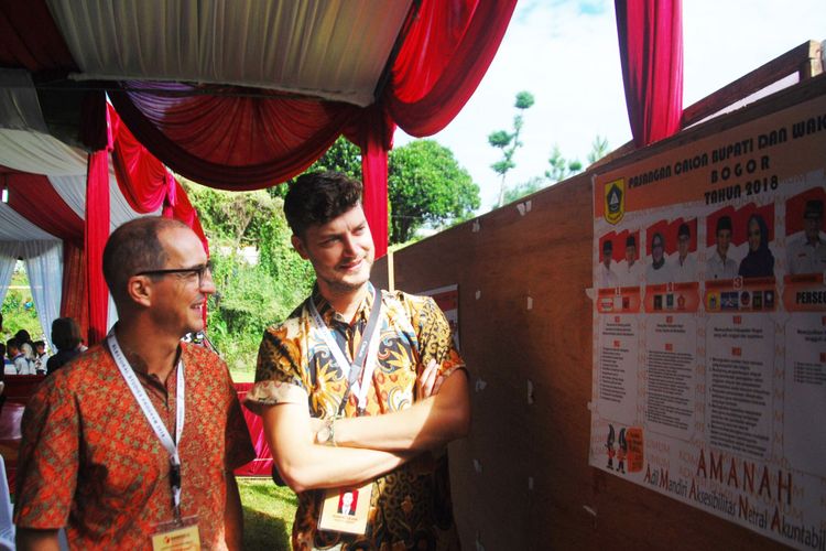 Dua anggota tim pengawas pemilu dari luar negeri sedang melihat poster foto pasangan calon kepala daerah di TPS 17, Desa Bojong Koneng, Kecamatan Babakan Madang, Kabupaten Bogor, Rabu (27/6/2018).