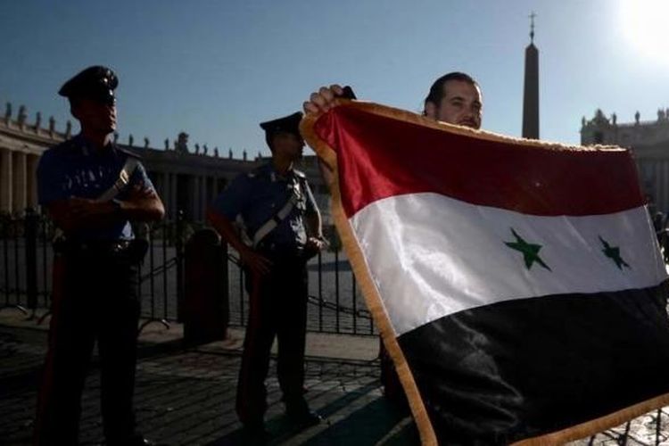 Seorang pria memegang bendera Suriah di Alun-alun St Peter's, Vatikan, 7 September 2013, menunggu kedatangan Paus Fransiskus memimpin doa bersama untuk perdamaian Suriah. Paus Fransiskus menyerukan kepada dunia agar puasa dan doa bersama untuk perdamaian Suriah dan menolak intervensi militer.