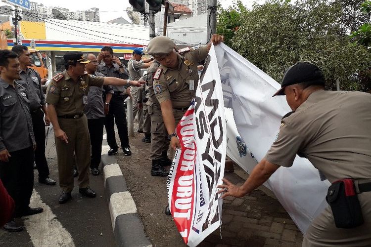 Satpol PP Jakarta Barat mencopot alat peraga kampanye yang dipasang di rambu lalu lintas dan petunjuk jalan di kawasan Srengseng, Kembangan, Jakarta Barat, Selasa (23/10/2018)