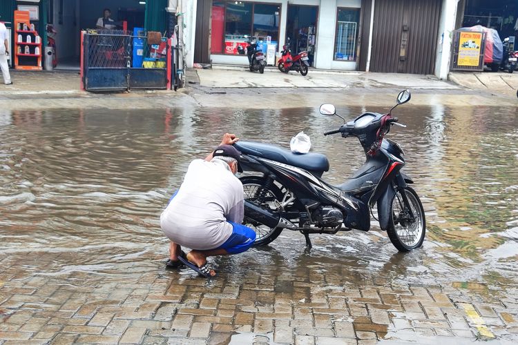 Meji (70), tampak mencuci sepeda motornya di genangan banjir, Jalan Raya Duta Pelni, Jumat (1/12/2023) siang.