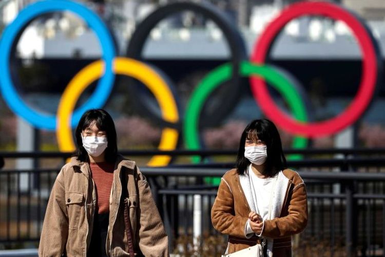 Dua warga berjalan di depan logo olimpiade di Tokyo, Jepang.