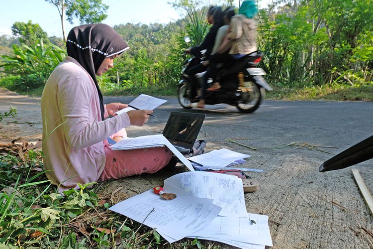 Teara Noviani a student at the University of Muhammadiyah Magelang takes the Mid-Semester Examination online on a roadside in the Menoreh mountain area in Central Java, Monday, July 20, 2020.