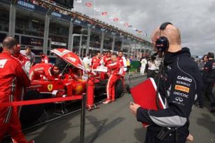 Kepala teknik Red Bull, Adrian Newey (kanan), melihat kru Ferrari sedang mengerjakan mobil mereka.