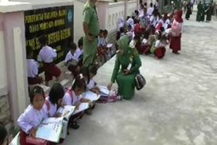 Ratusan siswa sd 55 majene terpaksa belajar di depan pingtu gerbang karena sekolahnya disegel warga.