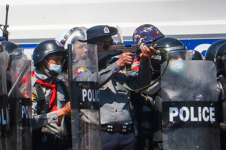 Seorang polisi (tengah) mengacungkan senapannya dalam bentrokan melawan massa yang ikut dalam demonstrasi menentang kudeta militer Myanmar di Naypyidaw, pada 9 Februari 2021.