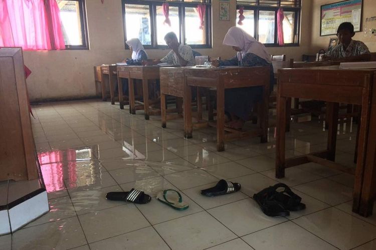Siswa SMP 3 Tirto, Pekalongan, Jawa Tengah mengerjakan soal ujian nasional dengan kondisi ruang kelas terendam banjir rob, Rabu (3/5/2017).