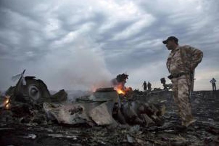 Seorang pria mengenakan seragam militer berada di dekat puing pesawat Malaysia Airlines yang membawa 295 orang penumpang dari Amsterdam ke Kuala Lumpur yang jatuh di Desa grabovo, Shaktarsk, timur Ukraina, Kamis (17/8/2014).