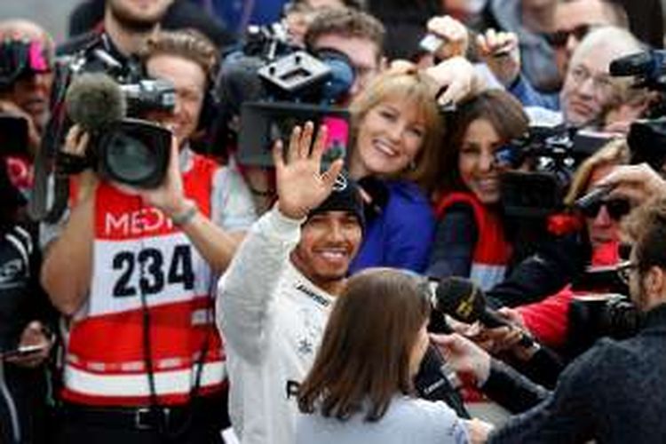 Pebalap Mercedes asal Inggris, Lewis Hamilton, melampai kepada para penggemar ketika sedang menjalani wawancara dengan para wartawan saat tes pramusim Formula 1 2016 di Sirkuit de Barcelona-Catalyunya, Senin (22/2/2016).