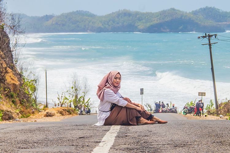 Seorang pengunjung Pantai Soge Pacitan berfoto di tengah jalan dengan latar belakang lautan.