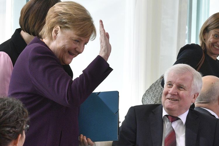 Kanselir Jerman Angela Merkel (kiri) tertawa seraya mengangkat tangannya pada 2 Maret 2020. Momen itu terjadi setelah Menteri Dalam Negeri Horst Seehofer menolak jabat tangan dengannya di tengah penyebaran virus corona.