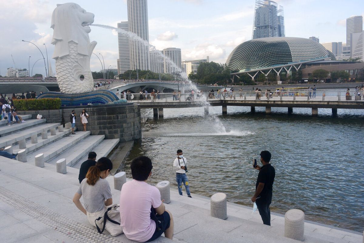 Seorang pria bermasker berpose untuk berfoto dengan latar belakang patung Merlion, Minggu, 26 September 2021, di Singapura. 