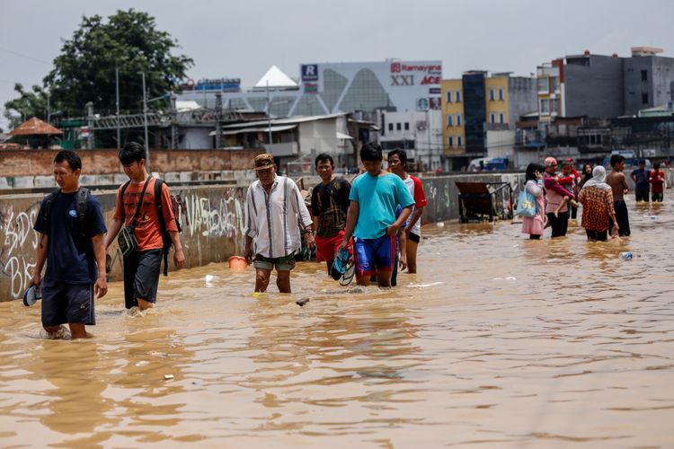 Warga berjalan melintasi banjir di Kampung Pulo, Jatinegara, Jakarta Timur, Selasa (6/2/2018). Banjir merendam ratusan rumah warga akibat luapan air dari Sungai Ciliwung.
