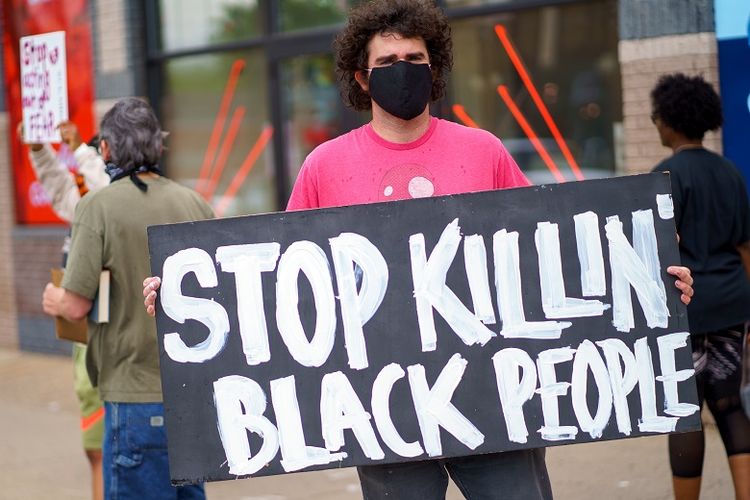 Seorang lelaki memegang plakat Stop Killing Black People ketika memprotes di dekat daerah tempat seorang petugas Kepolisian Minneapolis yang diduga membunuh George Floyd, pada 26 Mei 2020 di Minneapolis, Minnesota, Amerika Serikat.