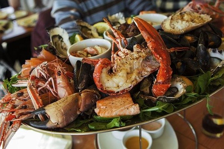Ilustrasi seafood platter, ada udang, lobster, kepiting, kerang dalam satu piring. 