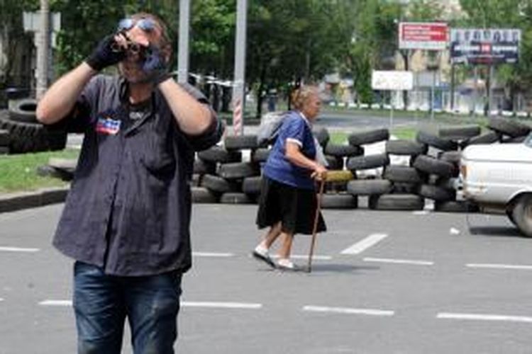 Seorang perempuan tua berjalan melintasi barikade pertahanan yang dibangun milisi pro-Rusia di kota Donetsk, Ukraina timur, sementara seorang anggota milisi menggunakan teropong memeriksa situasi di sekitar pos penjagaannya.