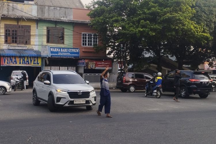 Pengatur lalu lintas informal atau pak ogah terlihat sedang membantu pengendara mobil untuk memutar arah di Jalan A.H Nasution, Kota Medan, Sabtu (16/8/2025)