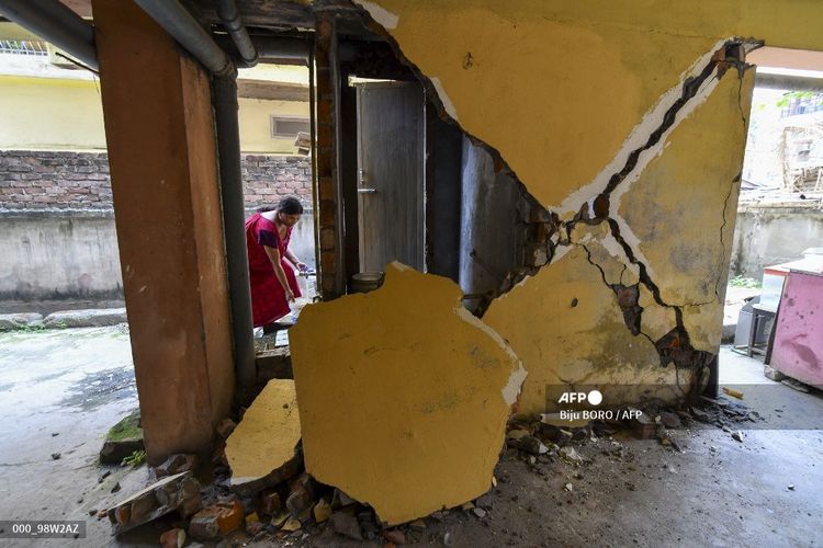 Seorang perempuan memunguti air dari keran dekat dinding yang retak di apartemen Guwahati, India,pada 28 April 2021. Sebuah gempa berkekuatan 6.0 mnegguncang timur laut India, merusak bangunan, namun belum dilaporkan adanya korban jiwa. Peristiwa ini terjadi saat India tengah menghadapi gelombang kedua Covid-19.