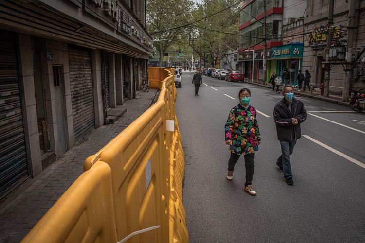 Warga berjalan memakai masker di jalanan yang masih dipasang pagar pembatas di Wuhan, China, 30 Maret 2020. Warga Wuhan bersiap memulai kembali aktivitasnya setelah lockdown dua bulan.