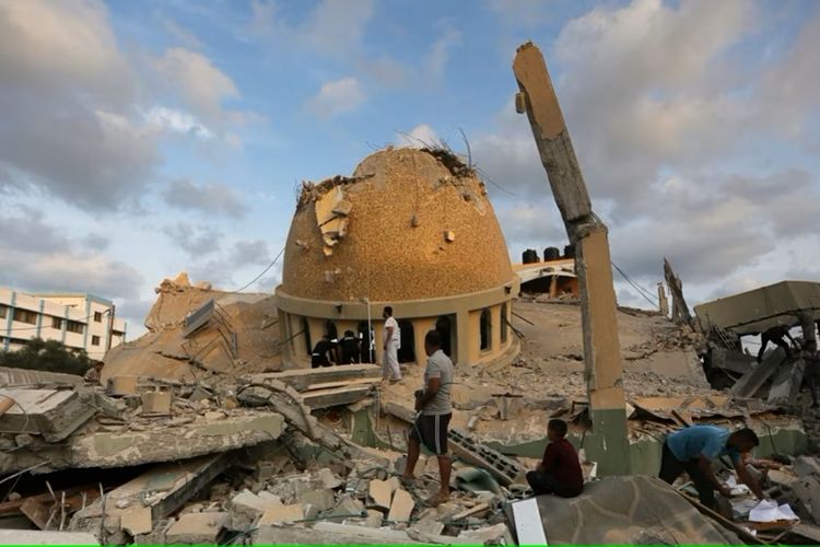Orang-orang berdiri di luar masjid yang hancur akibat serangan udara Israel di Khan Younis, Jalur Gaza, Minggu, 8 Oktober 2023.