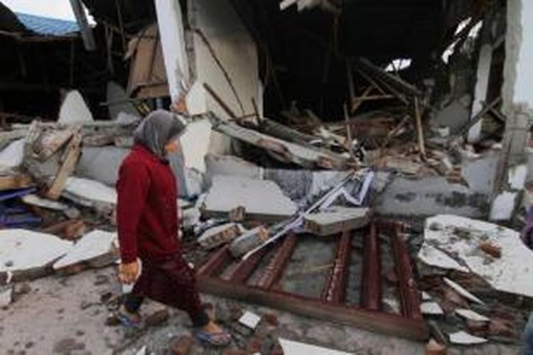 Warga melintasi di depan rumah yang hancur pasca-gempa di Blang Mancung, Aceh, 3 Juli 2013. Gempa berkekuatan 6.2 SR yang terjadi 2 Juli di Aceh, menghancurkan rumah dan mengakibatkan tanah longsor. 24 orang tewas dan ratusan terluka.
