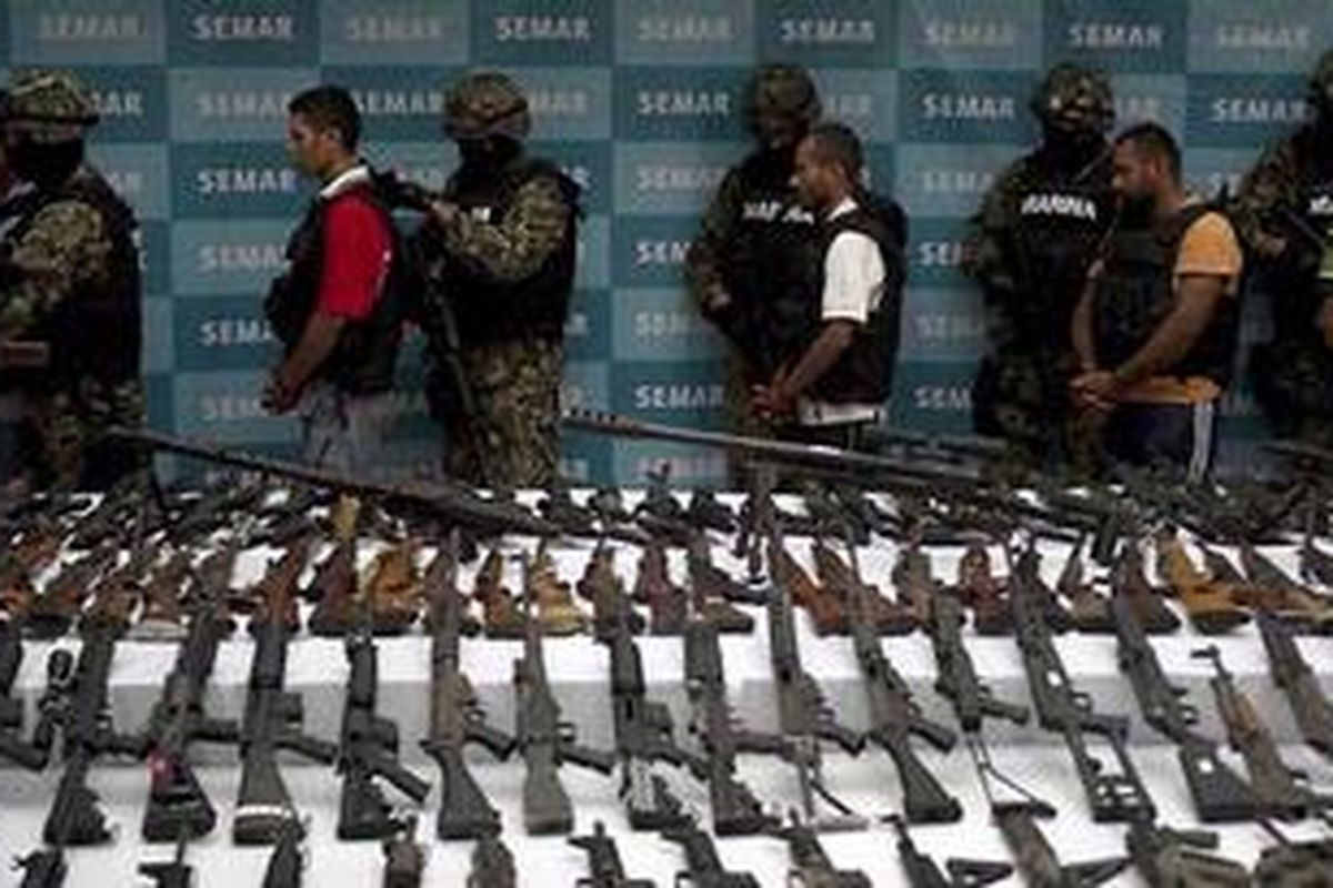 Anggota marinir Meksiko menggelandang sejumlah anggota kartel Zeta di depan puluhan senjata hasil sitaan. 