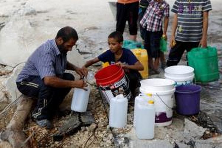 Seorang pria dan sejumlah anak-anak mengisi wadah-wadah plastik dengan air di wilayah Al-Shejaea, Jalur Gaza di tengah gencatan senjata selama 72 jam, setelah konflik bersenjata selama sebulan yang menewaskan lebih dari 1.800 warga Gaza.