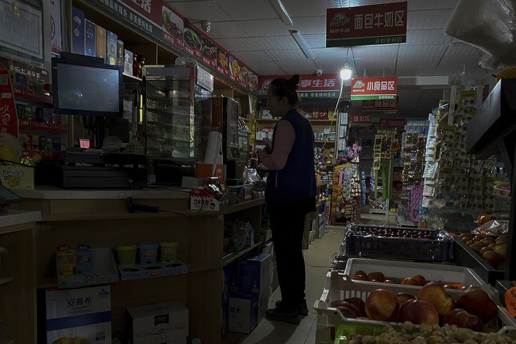 Krisis energi di China membuat seorang perempuan yang berbelanja di minimarket, hanya diterangi sebuah bohlam yang memakai aliran listrik dari generator. Foto diambil di Shenyang, provinsi Liaoning, China, pada Rabu (29/9/2021).