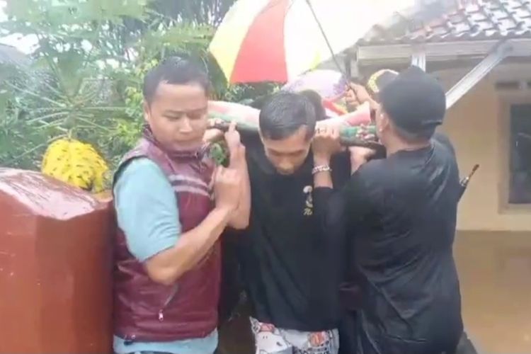 Kepala Desa Tanjungsari, Sukaresik, Kabupaten Tasikmalaya, Jawa Barat, bersama warga mengevakuasi warga yang sakit memakai tandu akibat rumahnya di gang saat banjir musiman di wilayah itu sambil diguyur hujan, Rabu (21/5/2025).
