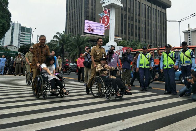 Gubernur DKI Jakarta Anies Baswedan mendorong pengguna kursi roda menyebrangi pelican crossing di Halte Bank Indonesia, Selasa (4/9/2018). 