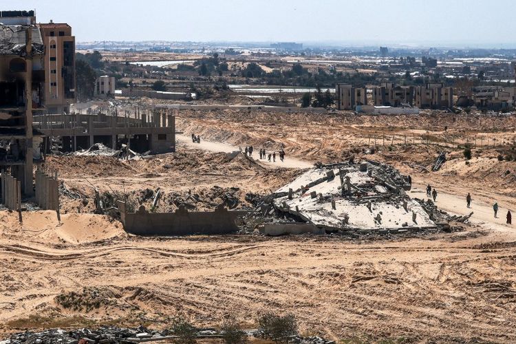 Orang-orang berjalan melewati bangunan yang rusak dan hancur di Khan Yunis pada 7 April 2024, setelah Israel menarik pasukan daratnya keluar dari Jalur Gaza selatan, Minggu (7/4/2024) hari ini.