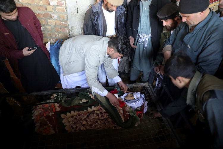 Beberapa pria berdiri di sekitar jenazah seorang anak laki-laki yang tewas serangan roket di Kabul, Afghanistan, Sabtu, 21 November 2020. Sebanyak 23 roket menghantam berbagai bagian ibu kota Afghanistan.