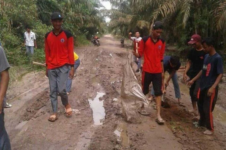Para pelajar SMA Negeri 1 Pulau Rimau, Kabupaten Banyuasin Gotong royong memperbaiki jalan rusak yang berlumpur akibat terkena hujan lebat.