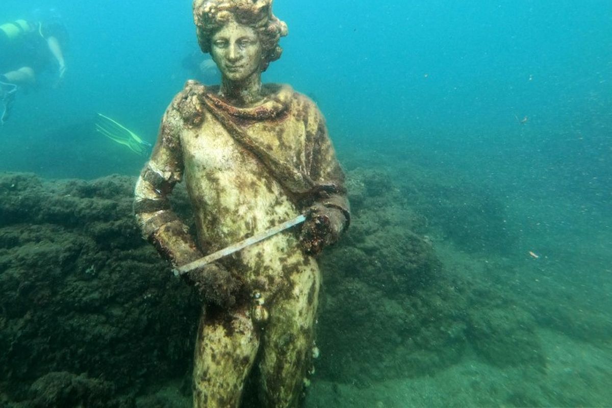 Dalam foto yang diambil pada 18 Agustus 2021 ini, pemandu selam menunjukkan kepada wisatawan patung asli yang ada di Museum Baiae, mewakili Dionysus dengan mahkota ivy di Nymphaeum of punta Epitaffio, kota Romawi kuno Baiae yang terendam di Baiae Underwater Taman.