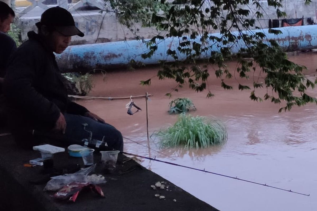 Warga memanfaatkan banjir di Jakarta untuk memancing di Kali Pesanggrahan, Rabu (1/1/2020).