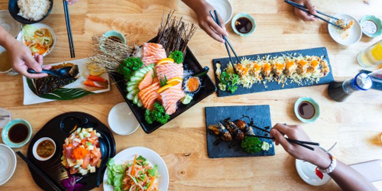 Satu set sushi di atas meja kayu di restoran Jepang, irisan salmon segar untuk menu sushi. Pesta teman atau keluarga makan sushi menggunakan batang bambu