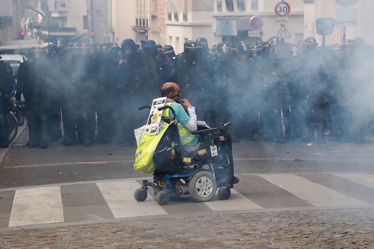Seorang pria dengan kursi roda berada di tengah kericuhan antara demonstran dan aparat keamanan saat aksi peringatan Hari Buruh Internasional 2019 di Paris, Rabu (1/5/2019). Aksi yang diperingati tahunan setiap tanggal 1 Mei itu digelar serentak di seluruh dunia untuk menyuarakan kesejahteraan bagi buruh.