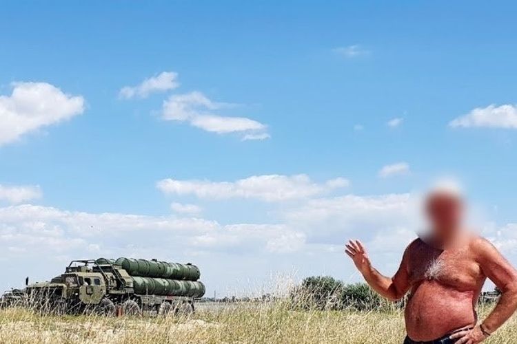 Gambar seorang pria dengan celana pendek ?Speedo? berdiri di pantai dengan sistem anti-pesawat S-400 Rusia sebagai latar belakangnya.
