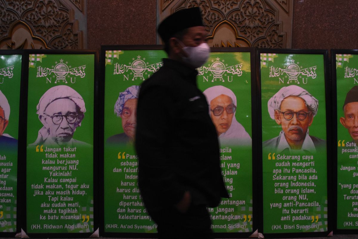 Kader NU melintas di dekat sejumlah foto para tokoh pendiri Nahdlatul Ulama saat diselenggarakannya Rapat Harian Syuriyah dan Harian Tanfidziyah Nahdlatul Ulama di Gedung PBNU, Jakarta, Selasa (7/12/2021). ANTARA FOTO/Indrianto Eko Suwarso/wsj.