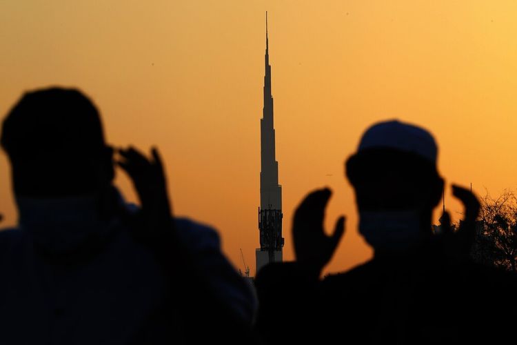 Dengan gedung tertinggi di dunia, Burj Khalifa, di latar belakang, pria Muslim yang mengenakan topeng untuk menahan penyebaran wabah virus corona melakukan sholat Idul Fitri menandai berakhirnya bulan suci Ramadhan di Dubai, Uni Emirat Arab, Kamis, Mei 13, 2021. 